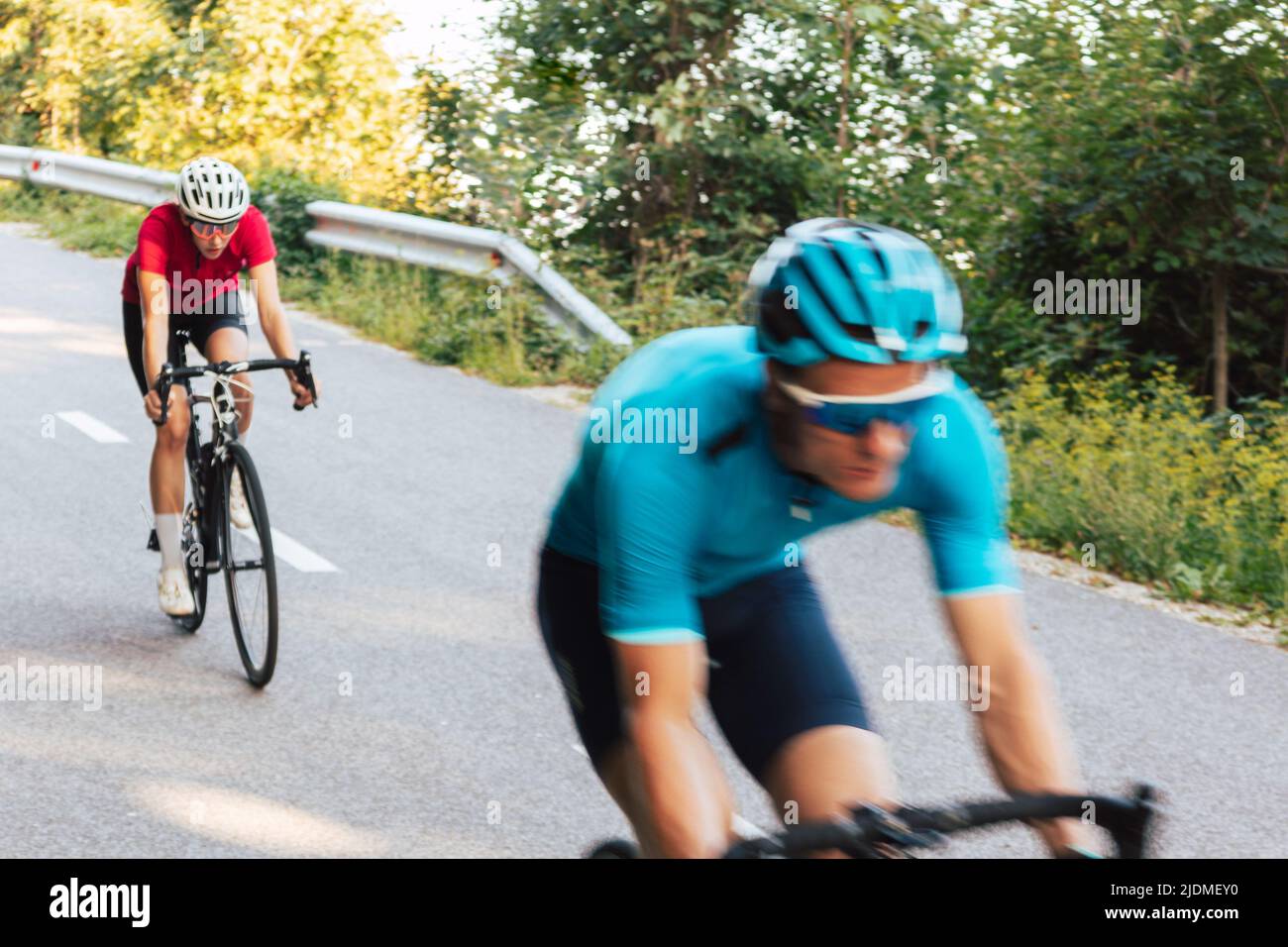 Movimento sfocato di due piloti su biciclette da corsa professionali che si discende velocemente sulla strada lastricata curvilinea attraverso la foresta Foto Stock