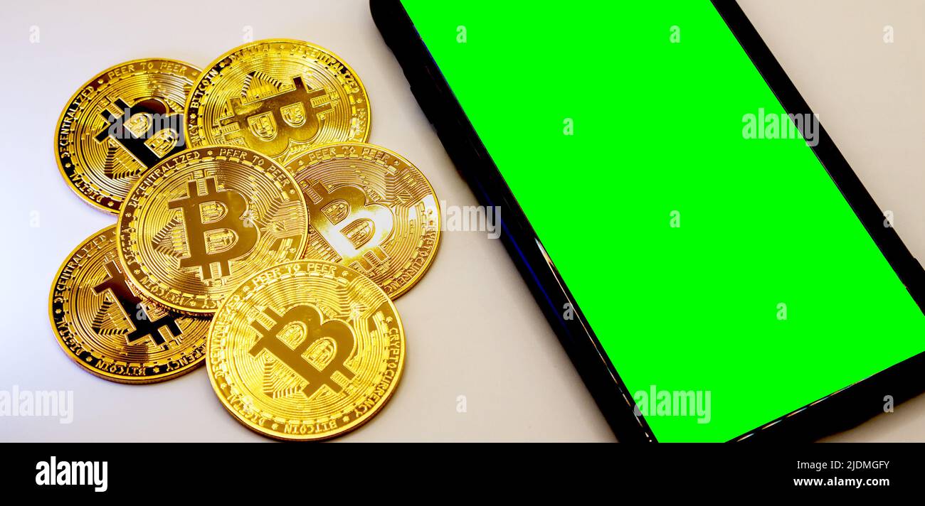 Monete Bitcoin in metallo dorato con uno smarthphone accanto ad esso, spazio copia area schermo verde Foto Stock
