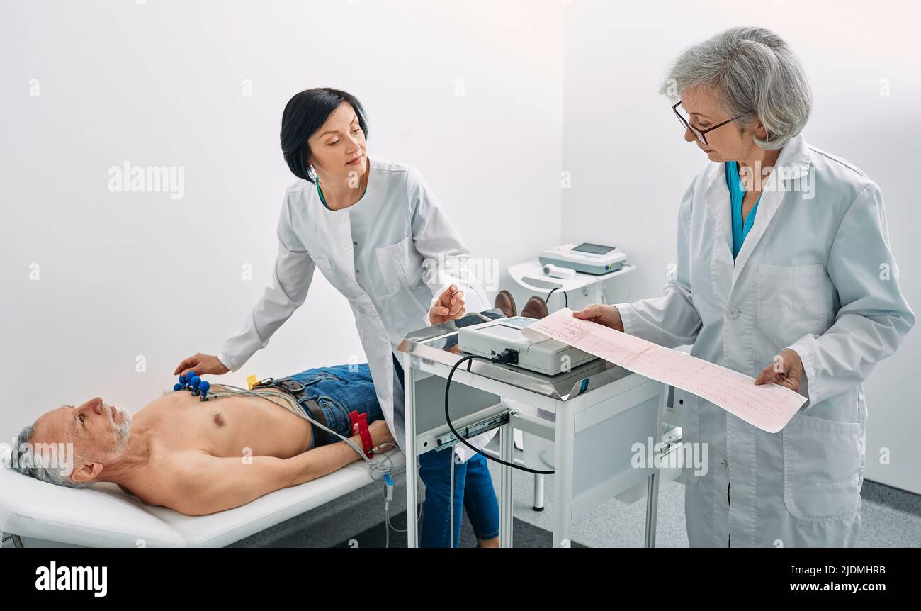 Test del cardiogramma. Il paziente anziano di sesso maschile riceve il monitoraggio della frequenza cardiaca mediante un'apparecchiatura di elettrocardiogramma con due medici cardiologi Foto Stock
