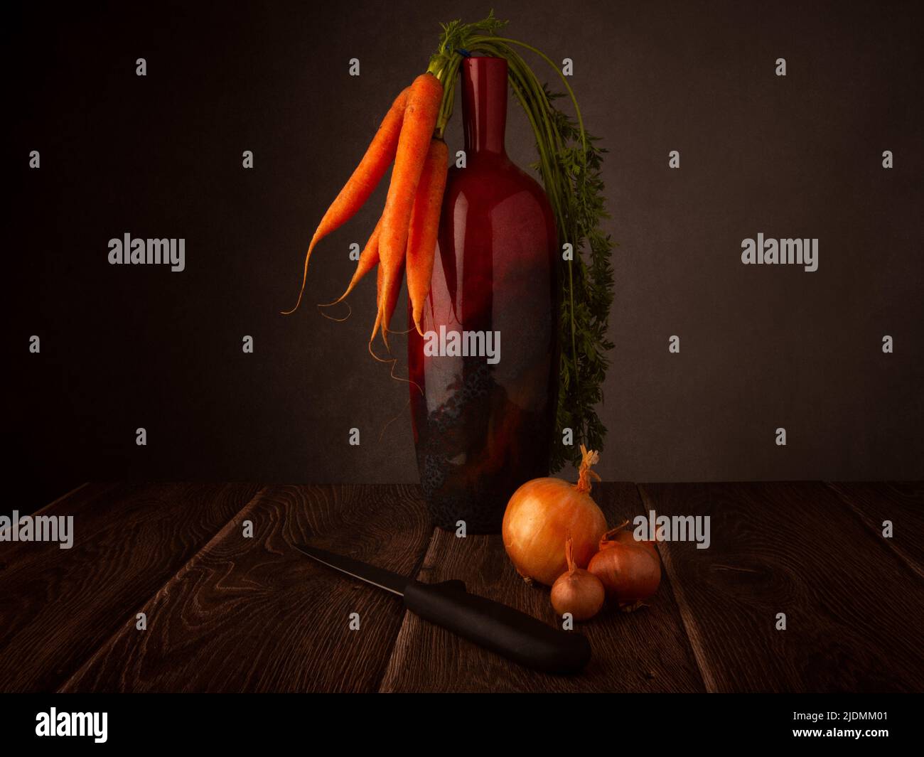 Ancora vita di carote biologiche poggiate su un vaso, cipolle e un coltello su un tavolo di legno scuro con sfondo scuro copia del tor Foto Stock