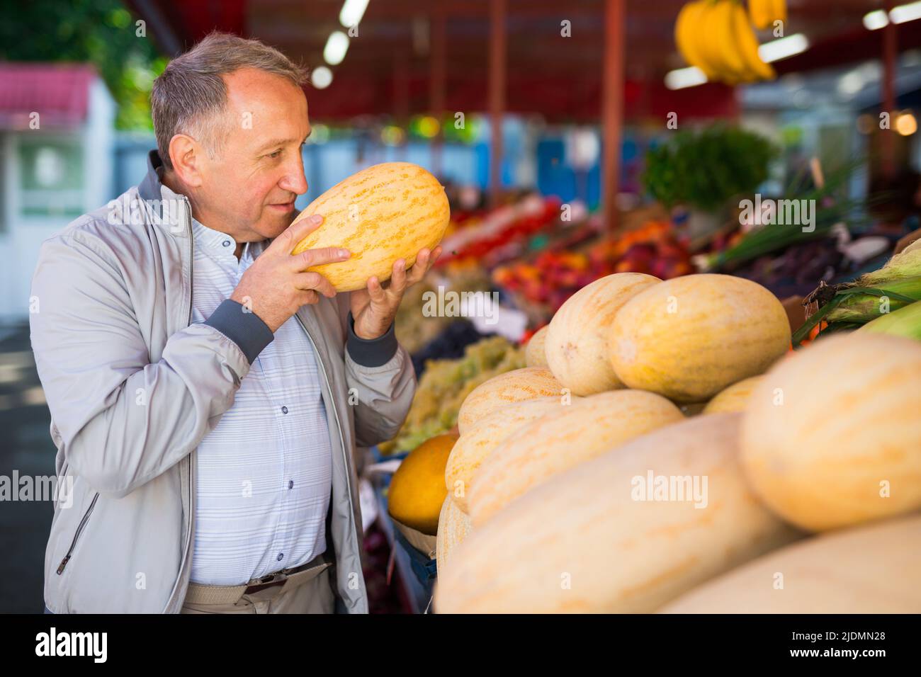 Uomo che sceglie i meloni nel negozio di frutta Foto Stock