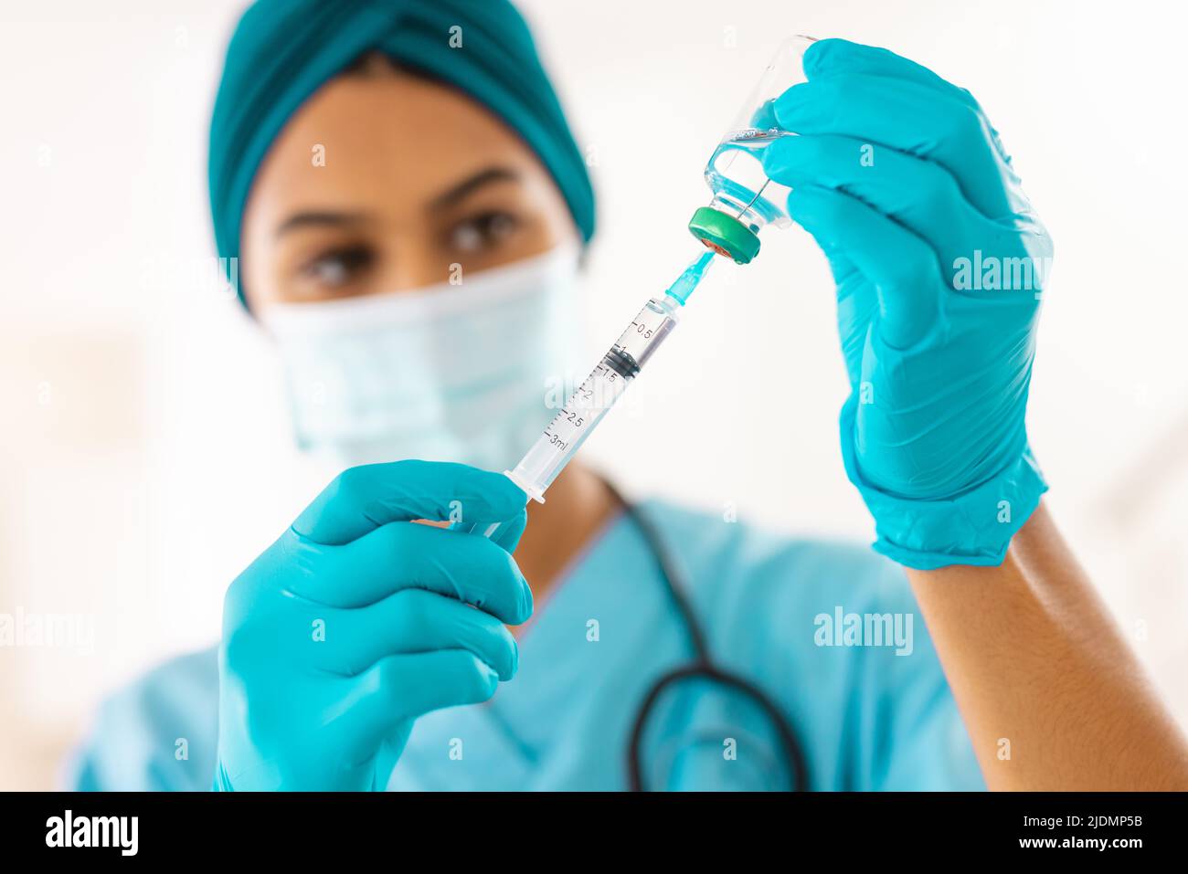 Medico giovane biracale in maschera protettiva per il viso con siringa in clinica Foto Stock