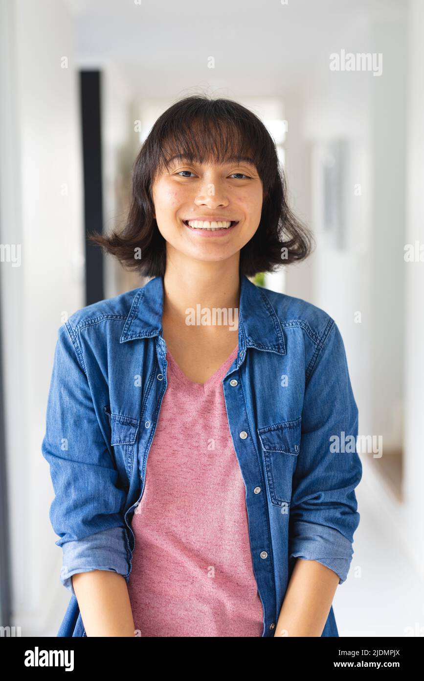 Ritratto di giovane donna asiatica sorridente con capelli corti indossando giacca in denim in piedi a casa Foto Stock