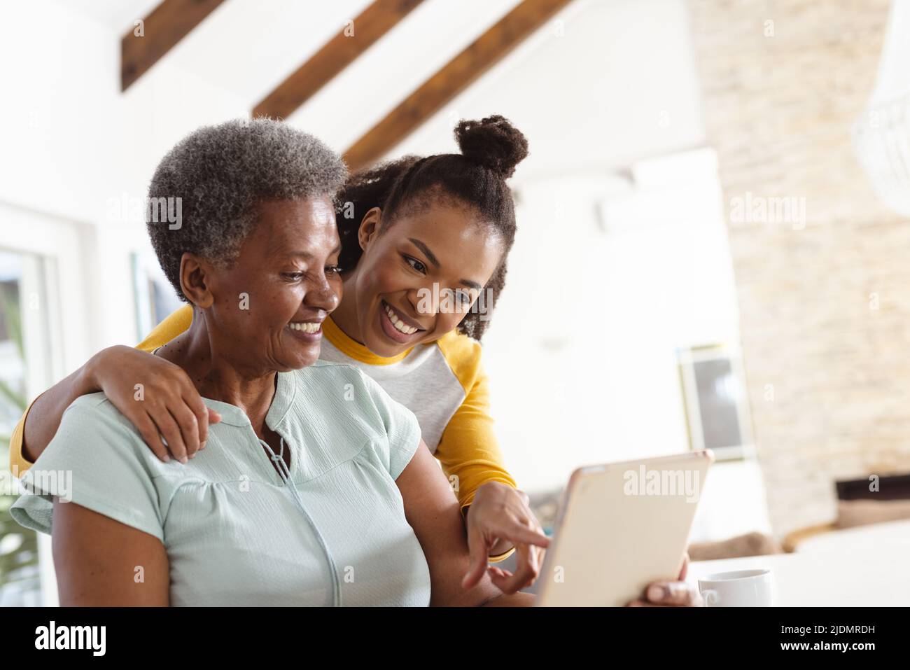 Sorridente figlia afroamericana che punta al computer portatile che è usato da madre anziana sul tavolo Foto Stock