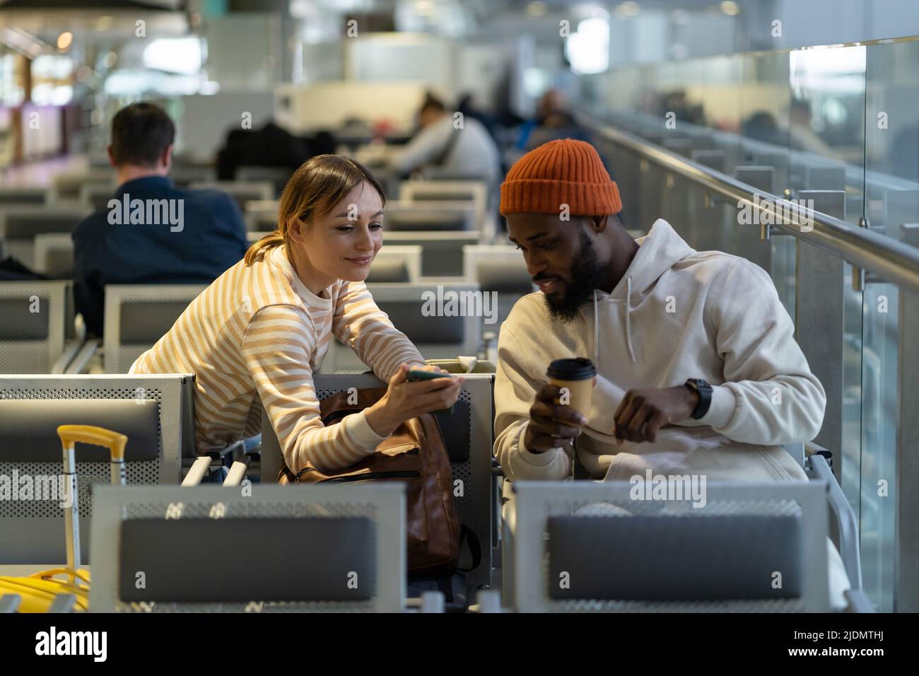 Maschio hipster nero e femmina caucasica bella guardando il telefono mentre si aspetta il volo in aeroporto. Foto Stock