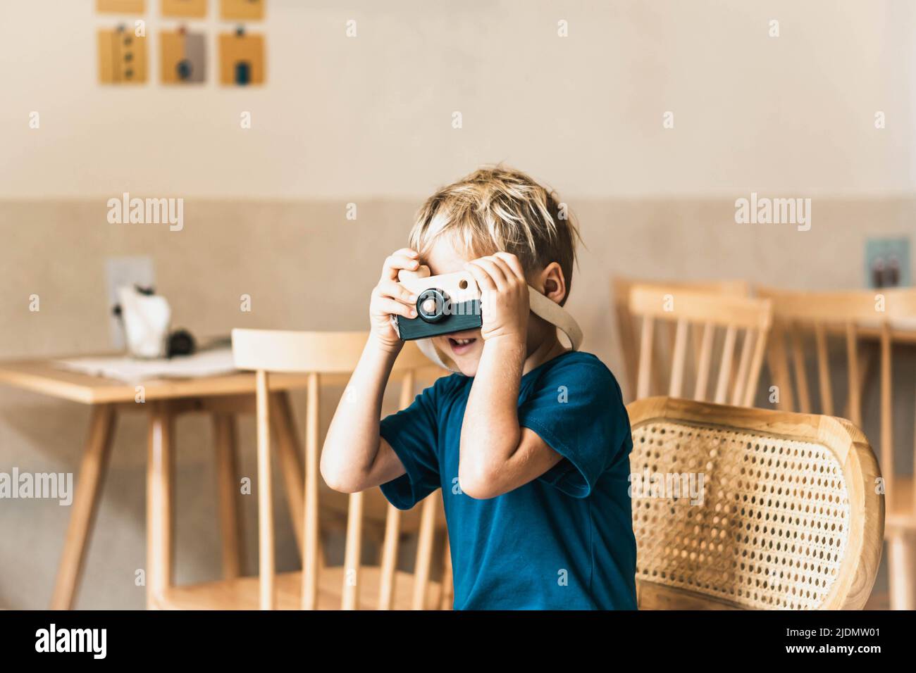 Carino sorriso felice ragazzino giocare a macchina fotografica in legno fatto a mano, tenere il giocattolo in mani. Attività artigianali artistiche. Abilità di sviluppo dei bambini di prescolare Foto Stock