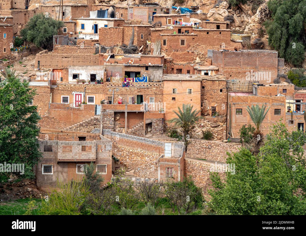 Villaggio di famiglia berbero con pareti in pietra e argilla, e porte, tetti e recinzioni costruite da rami di albero. Montagne dell'Atlante e cielo blu a bac Foto Stock