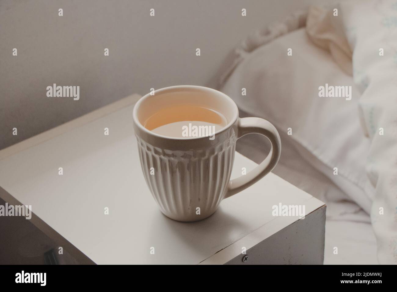 semplice tazza bianca con tè accanto al letto Foto Stock
