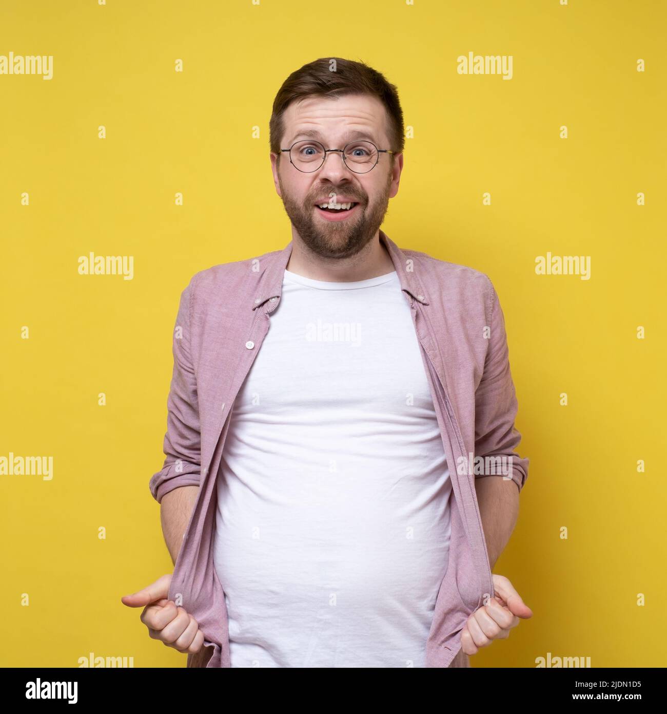 Uomo in sovrappeso che tiene la sua camicia mostrando il grasso extra del ventre e fremente contently. Concetto di corretta alimentazione e stile di vita sano. Foto Stock