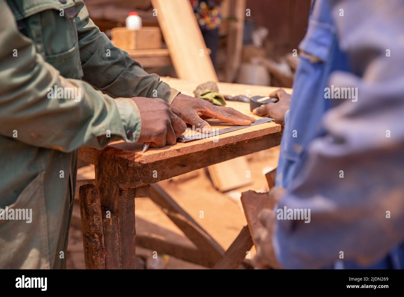 Primo piano delle mani di due carpentieri che effettuano le misurazioni su un asse di legno durante il lavoro Foto Stock