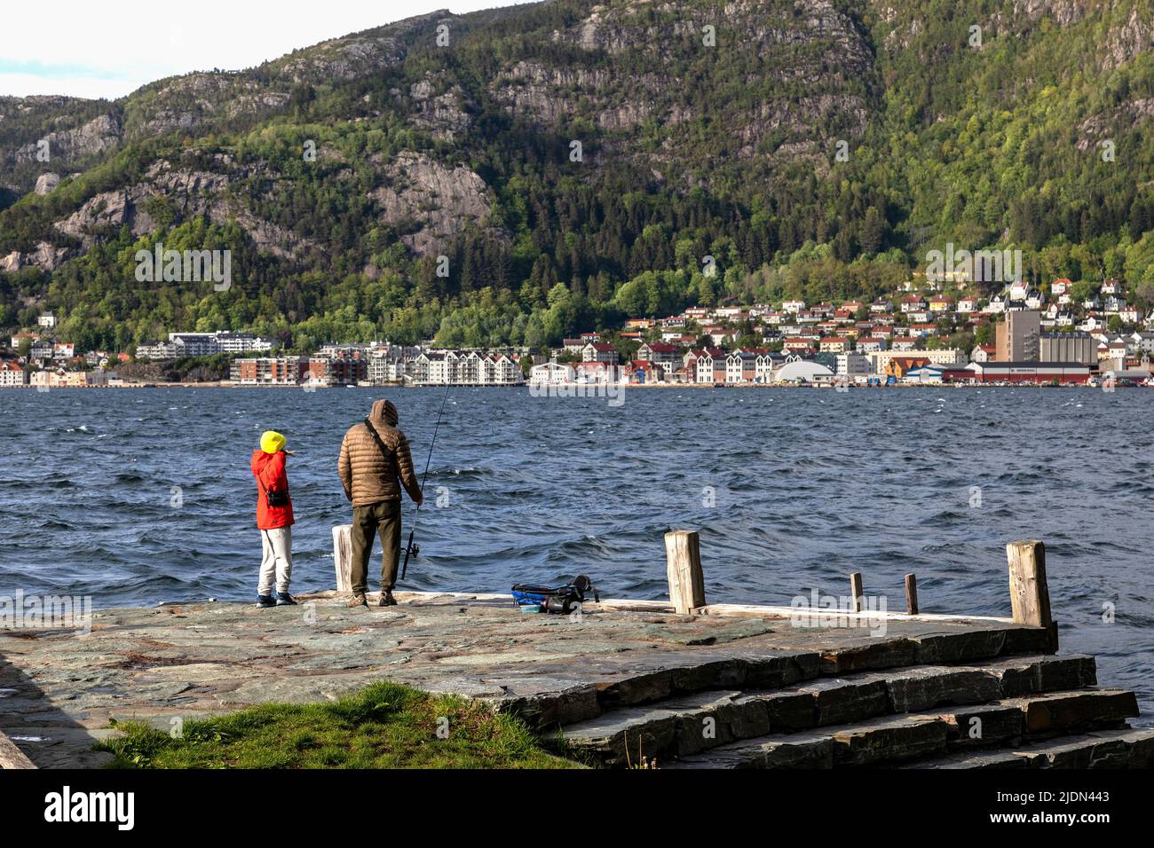 Due persone pescano a Ballastbryggen a Nornespynten all'inizio dell'estate. Nordnes Park, Bergen, Norvegia. Vista verso Sandviken Foto Stock