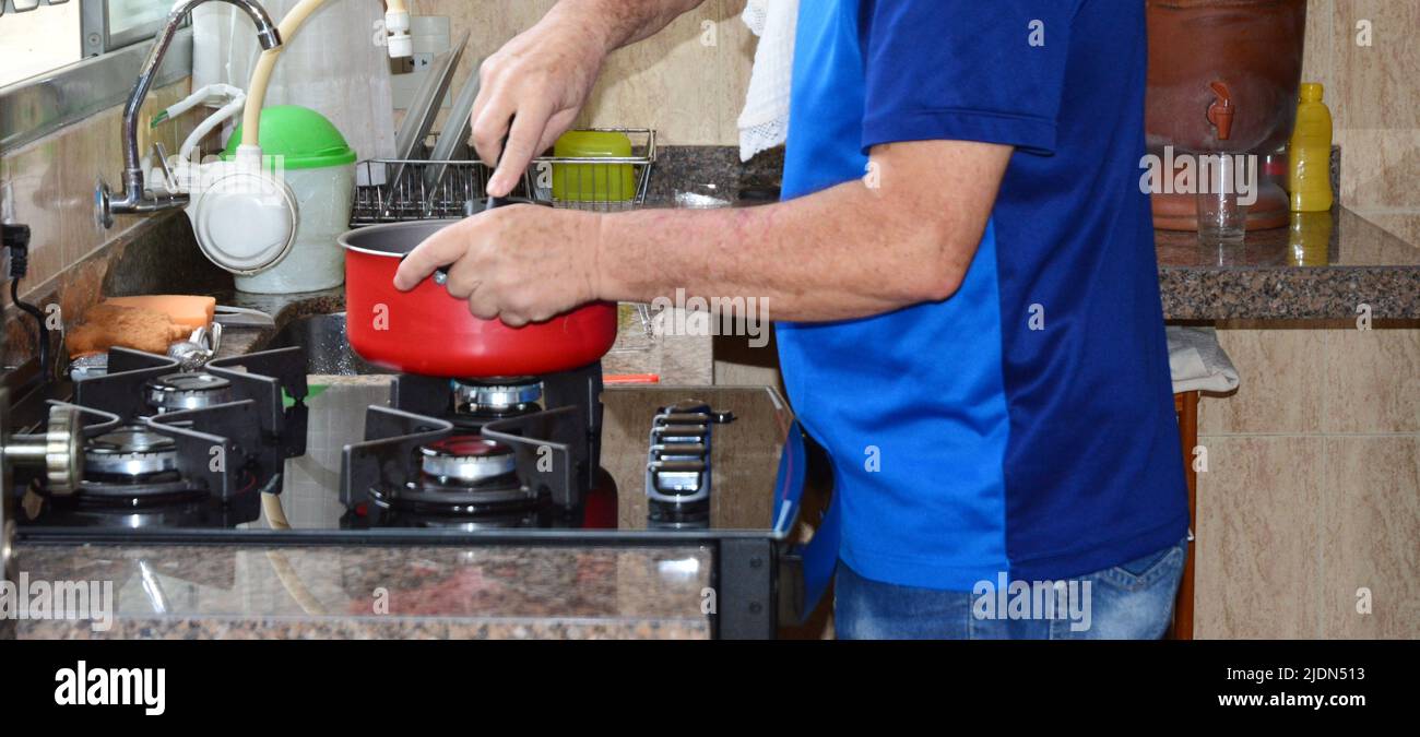 Uomo che fa lavori di casa, preparando la cena a casa su pentola rossa e stufa Brasile, Sud America, foto panoramica, raccolto intenzionale, vista laterale Foto Stock