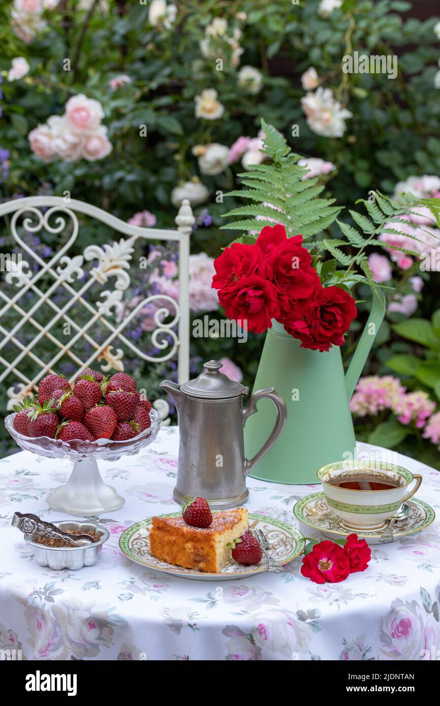 decorazione capace con pezzo di torta, fragole, porcellana vintage e bouquet di rose in giardino estivo Foto Stock