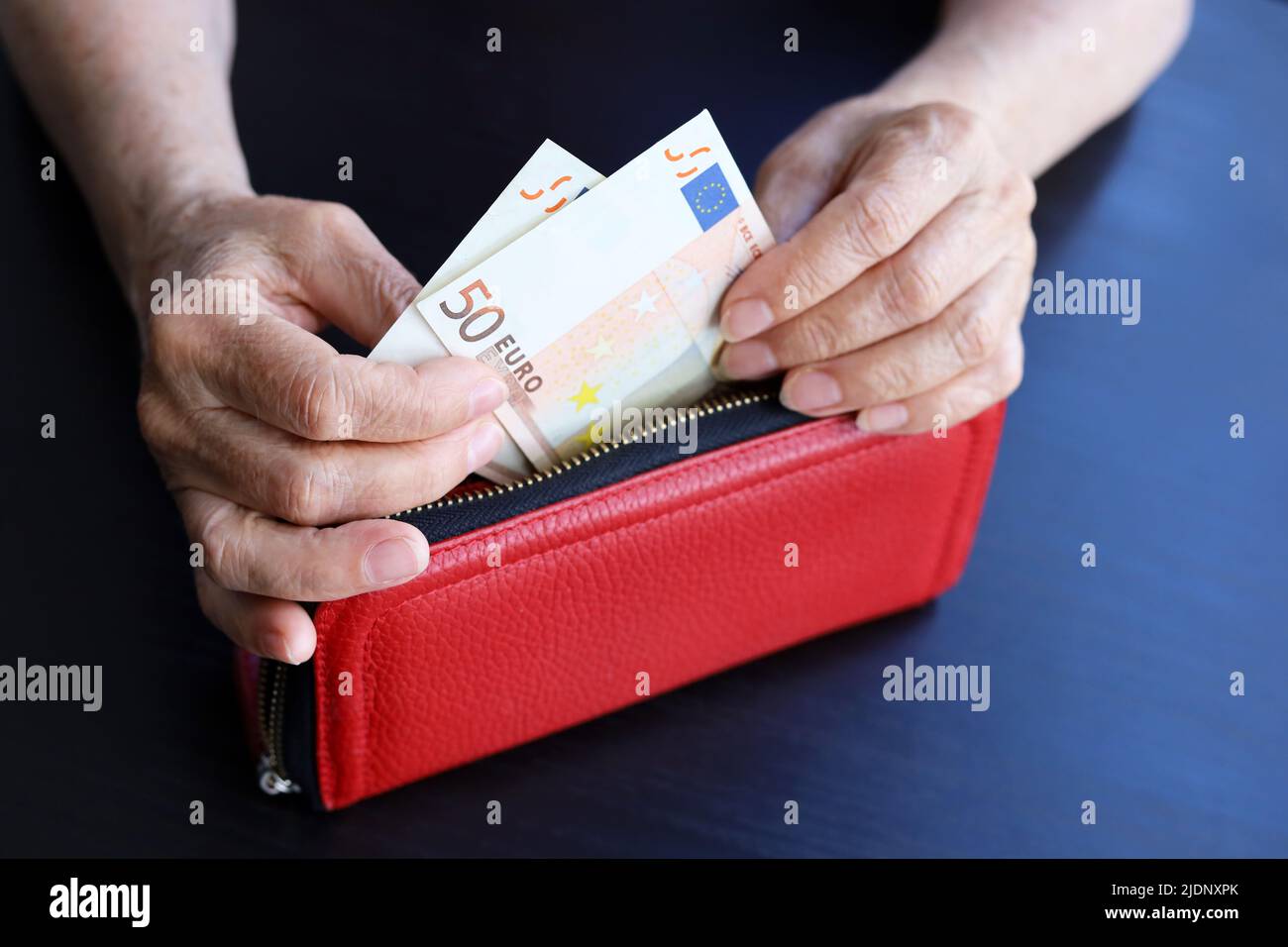 Donna anziana prende le banconote in euro dal portafoglio rosso, rughe donna mani primo piano. Concetto di previdenza e assistenza, risparmio, pensionamento Foto Stock
