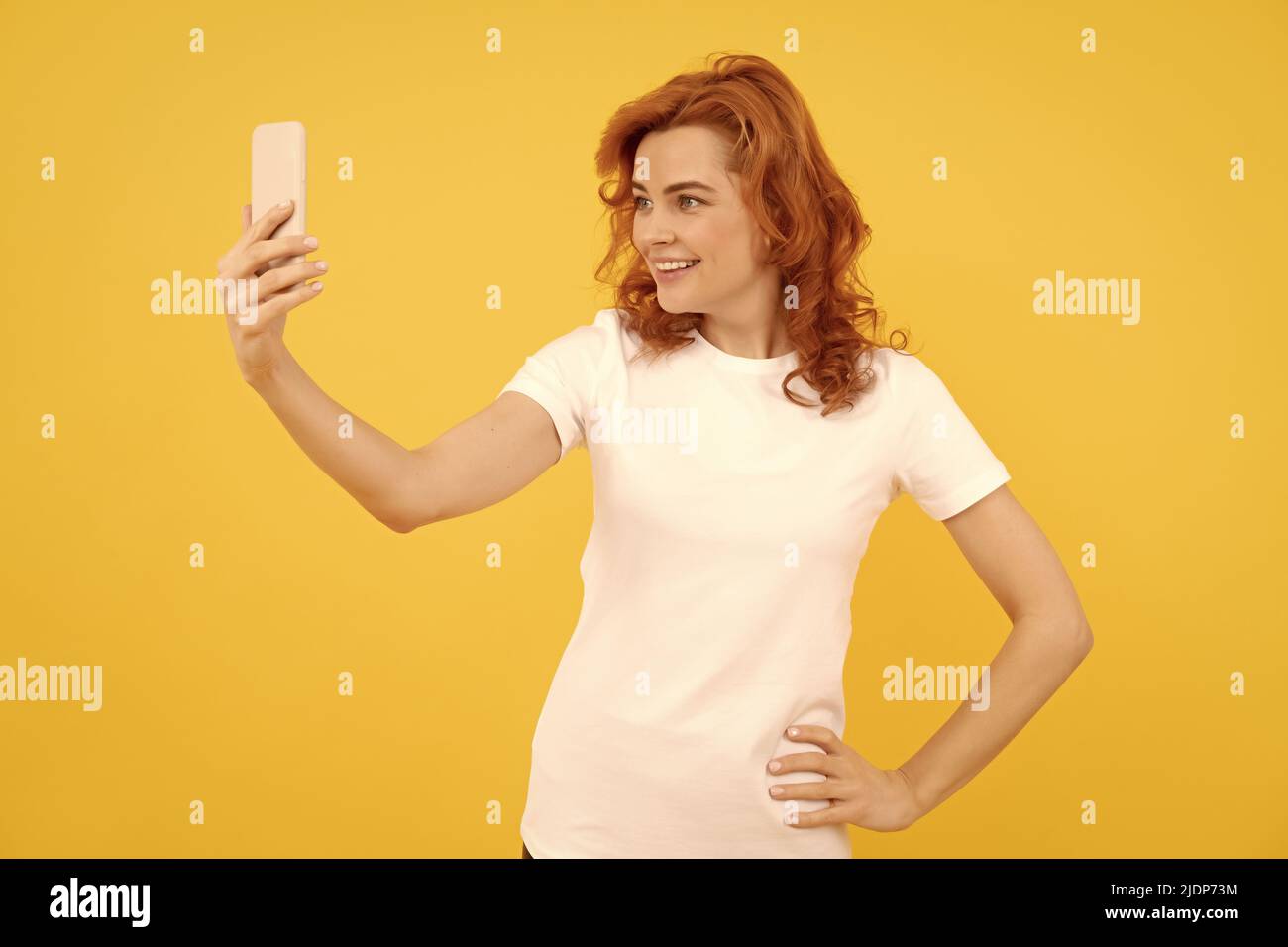 Felice ragazza sorriso a cellulare fotocamera telefono sfondo giallo, selfie video Foto Stock