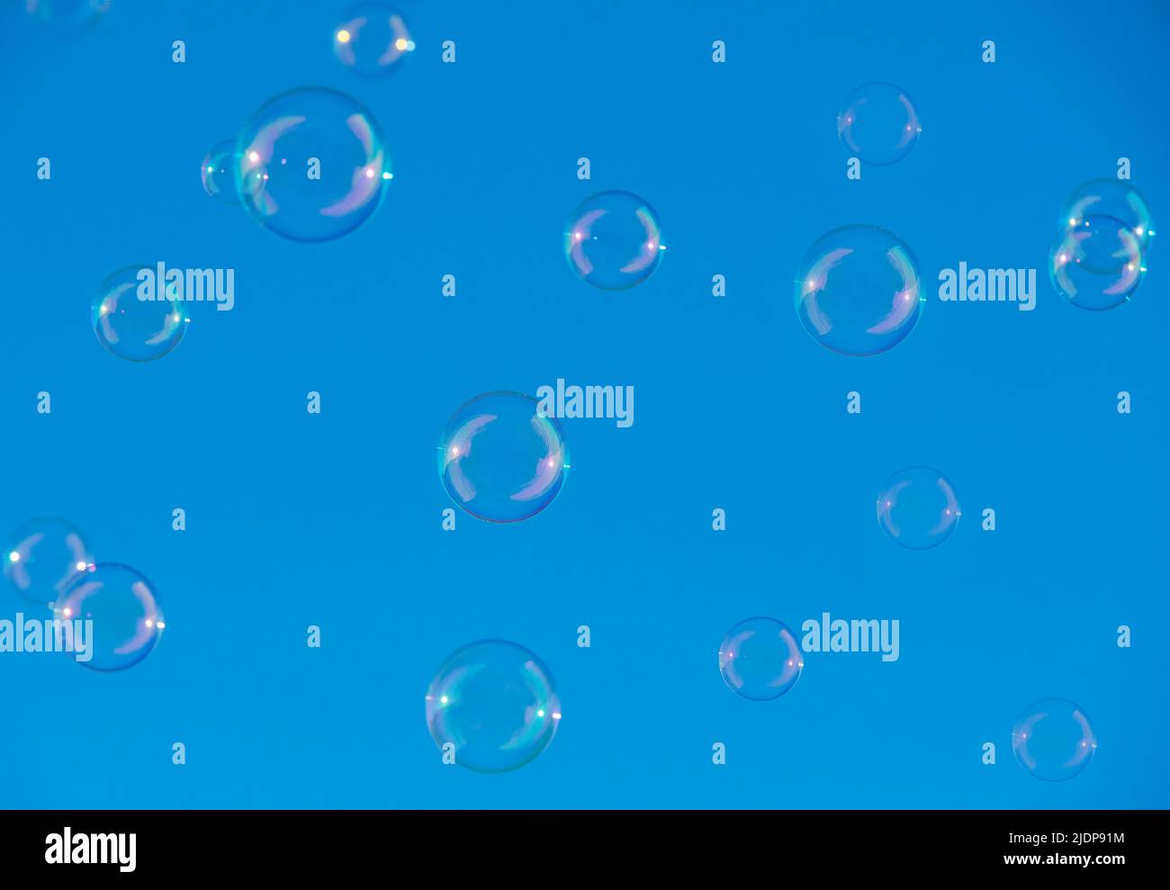 le bolle di sapone puri e iridescenti galleggiano nell'aria con un bel cielo blu chiaro sfondo. Foto Stock