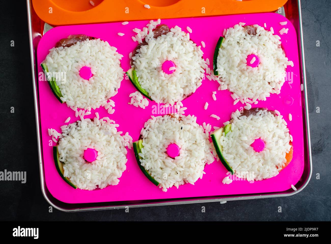 Preparazione del sushi a forma di ciambella in una muffa di silicone: Il riso di sushi pressato in una muffa di ciambella sopra il pesce fresco e le verdure Foto Stock