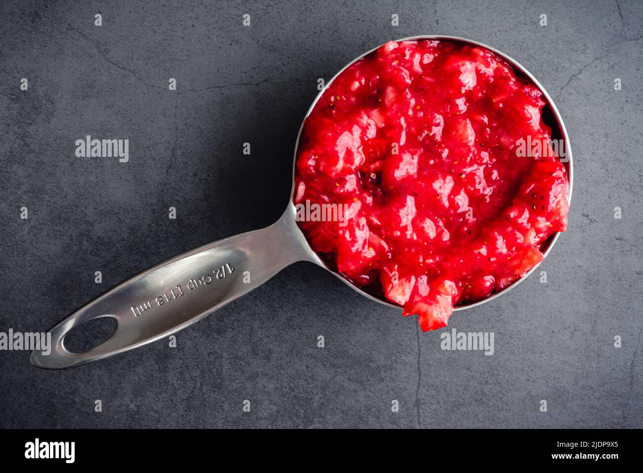 Tazza di misurazione riempita con purea di fragole: Vista dall'alto di una tazza di misurazione in metallo riempita con fragole di canna Foto Stock