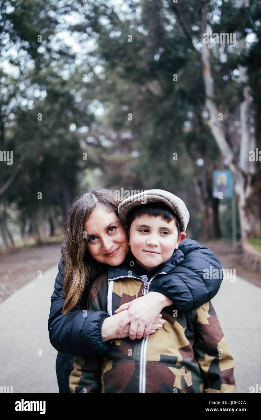 Giovane madre bionda che abbraccia il suo giovane figlio in una strada del parco. Famiglia con un solo genitore Foto Stock