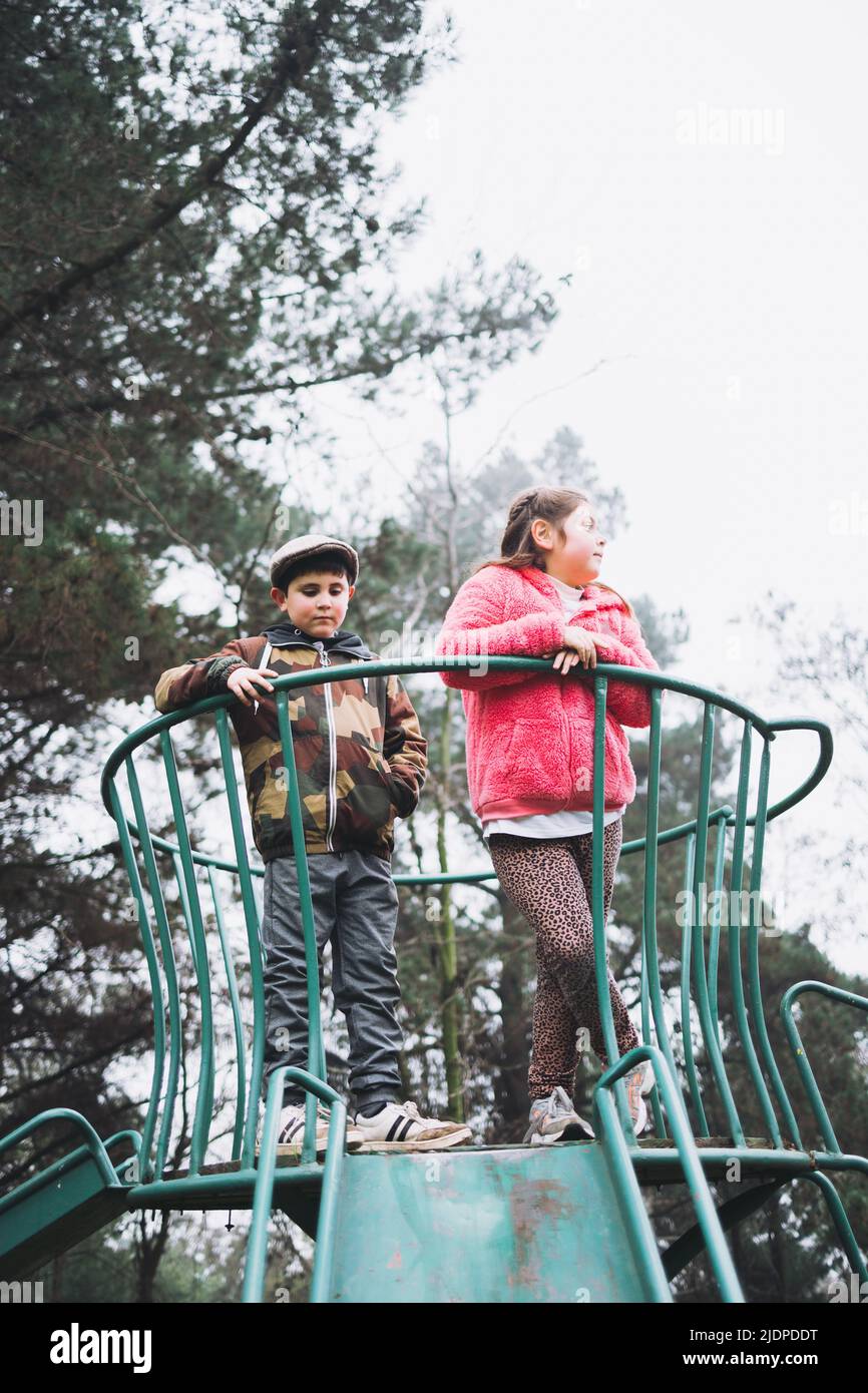 Due bambini che giocano in uno scivolo in un parco giochi verde. Attività ricreative al parco. Verticale Foto Stock