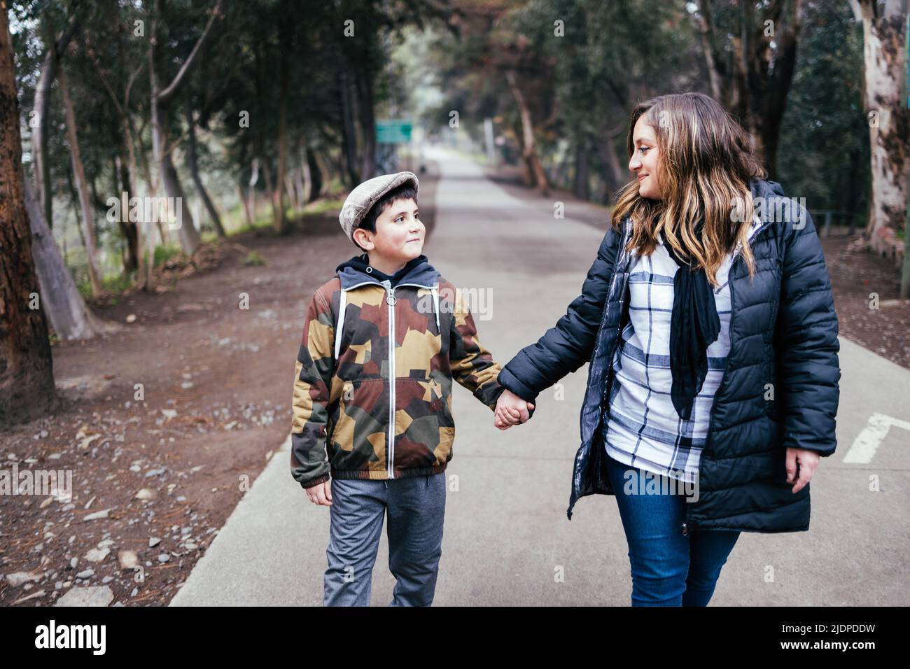 Giovane madre bionda che cammina e parla con suo figlio in una strada del parco. Famiglia con un solo genitore Foto Stock