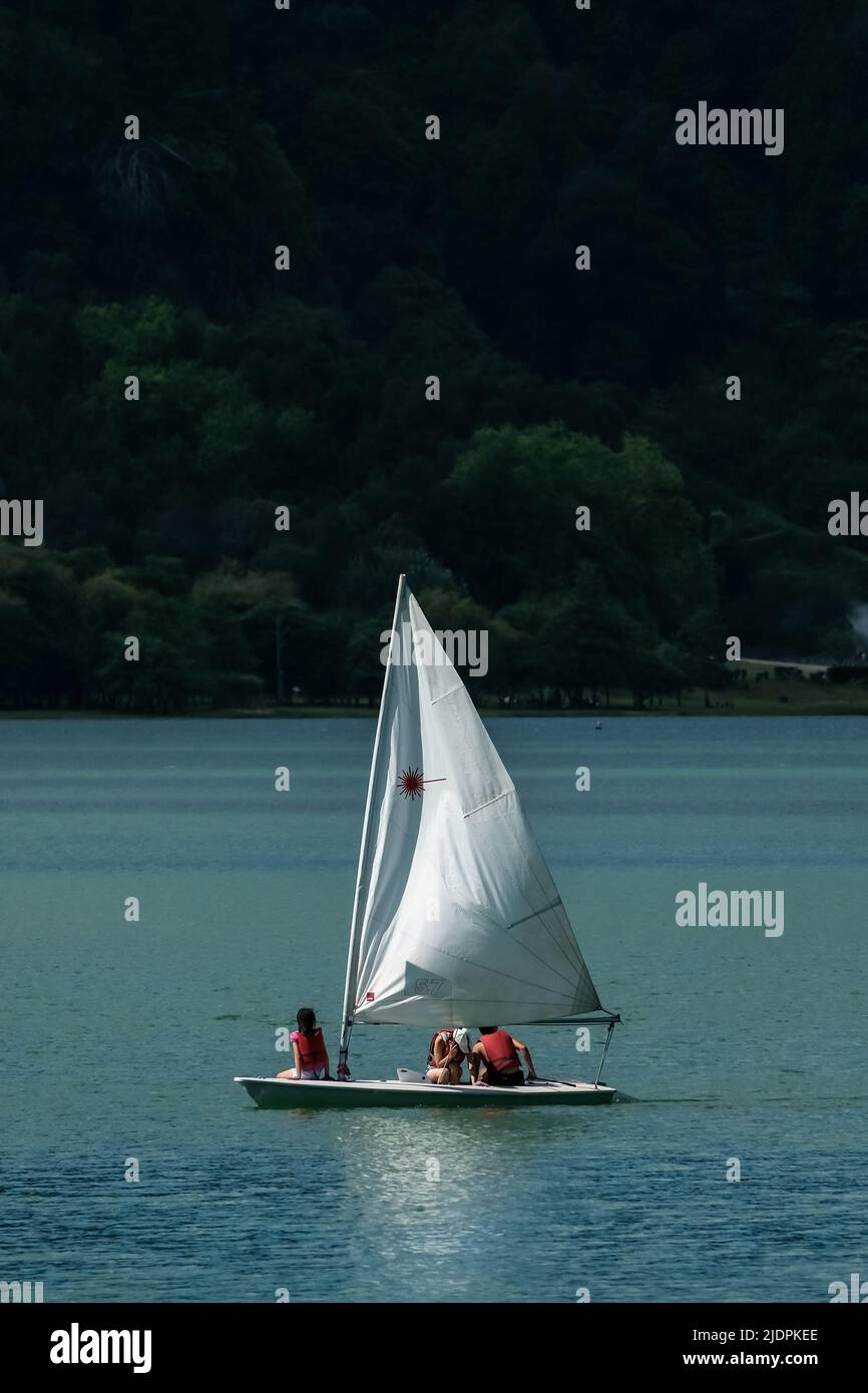 Piccola barca a vela nel lago Furnas - 'Lagoa das Furnas' -, con vegetazione verde sullo sfondo, isola di São Miguel nelle Azzorre, Portogallo Foto Stock