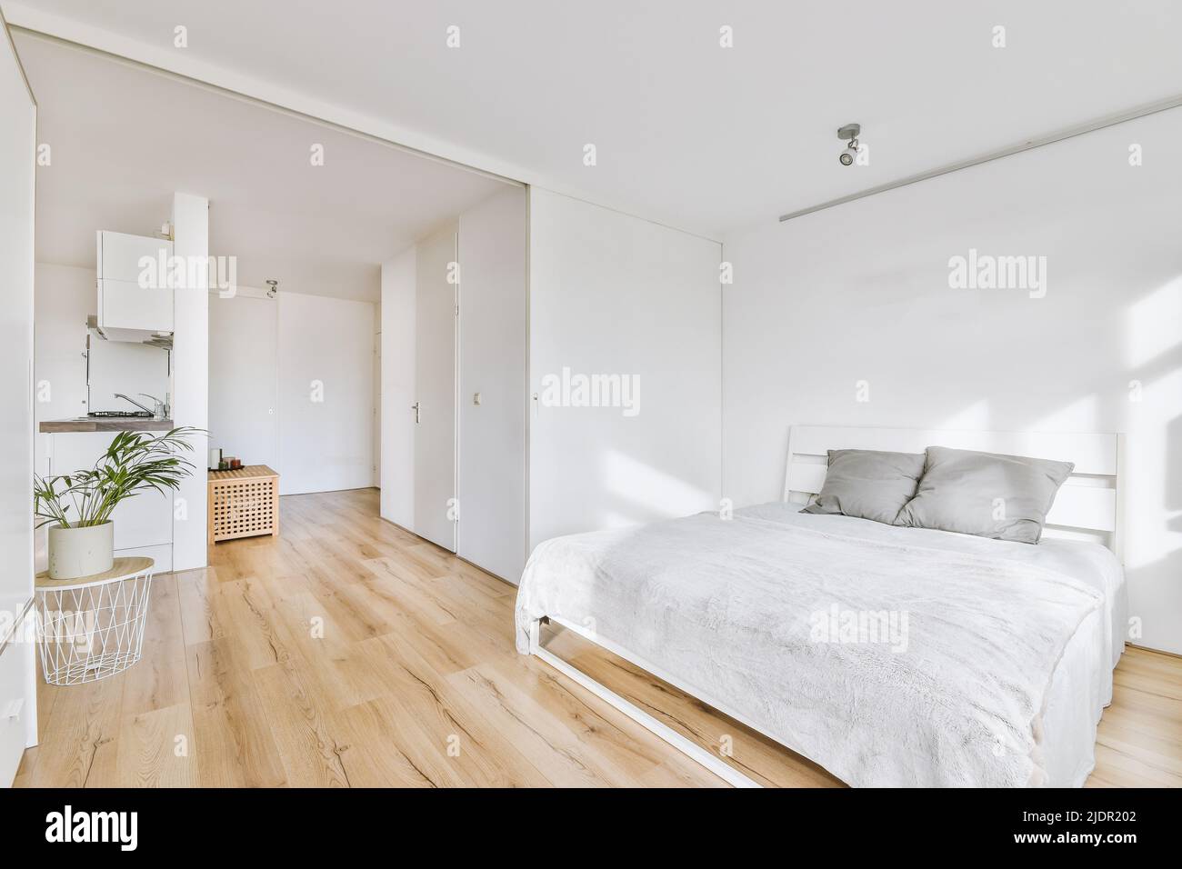 Design minimalista degli interni della camera da letto con morbido letto con cuscini grigi contro la parete e guardaroba bianco incorporato con luce naturale del sole Foto Stock