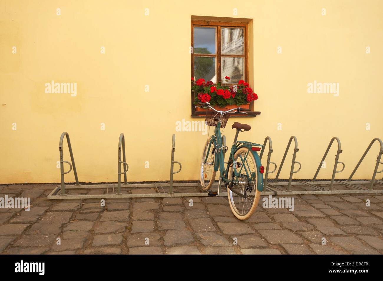bicicletta verde parcheggiata da una finestra con fiori rossi Foto Stock