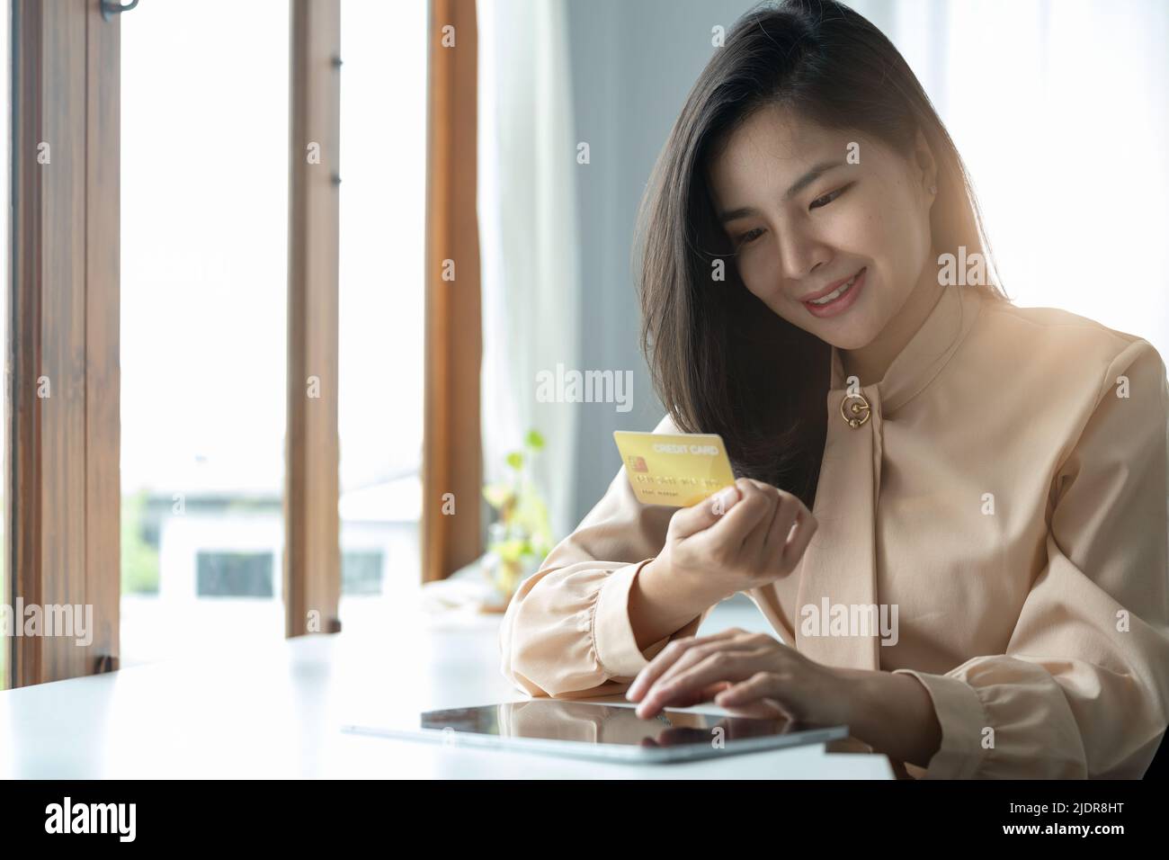 Giovane donna asiatica sorridente usando il tablet che acquista shopping online con carta di credito nel soggiorno di casa. Stile di vita latino e ispanica etnia donne a. Foto Stock
