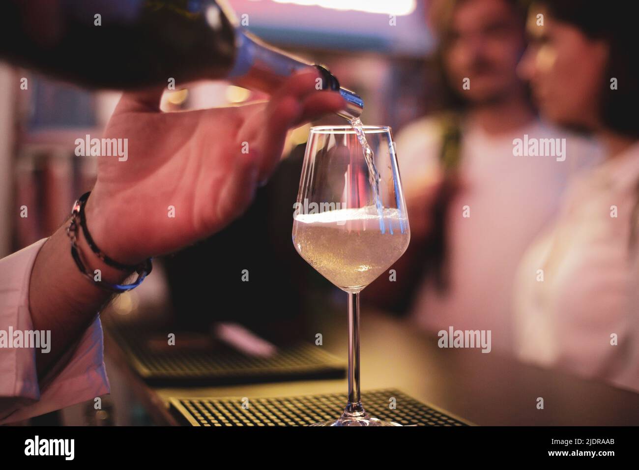 Dettagli poco profondi di campo (fuoco selettivo) con vino frizzante versato in un bicchiere in un bar. Foto Stock