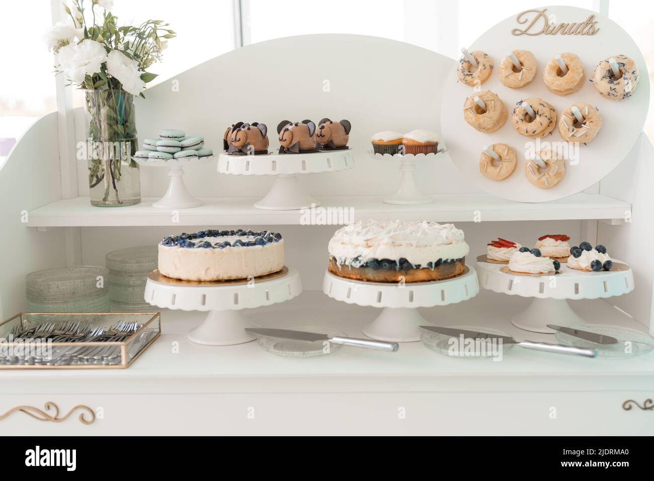 Serve ciambelle decorate, torte alla bacca, biscotti e cupcake cremosi su vassoio, sfondo bianco. Dolci al forno, festa dell'evento. Pasticceria fatta in casa Foto Stock