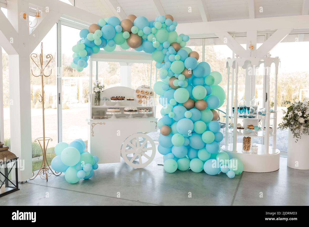 Stand festivo con deliziosi dessert e bevande fresche, palloncini blu arco nella sala banchetti bianca. Opere d'arte, sala decorata, celebrazione dell'evento. Vacanza Foto Stock