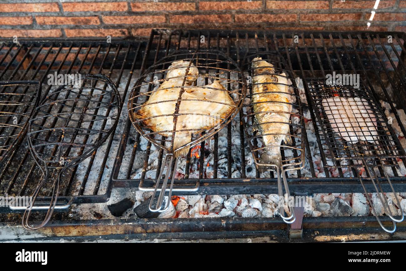 Pesce fresco grigliando su vecchio carbone parrillas pesce bianco spigola e rombo, costruire al di fuori degli edifici in piccolo villaggio di pescatori Getaria, basco Foto Stock