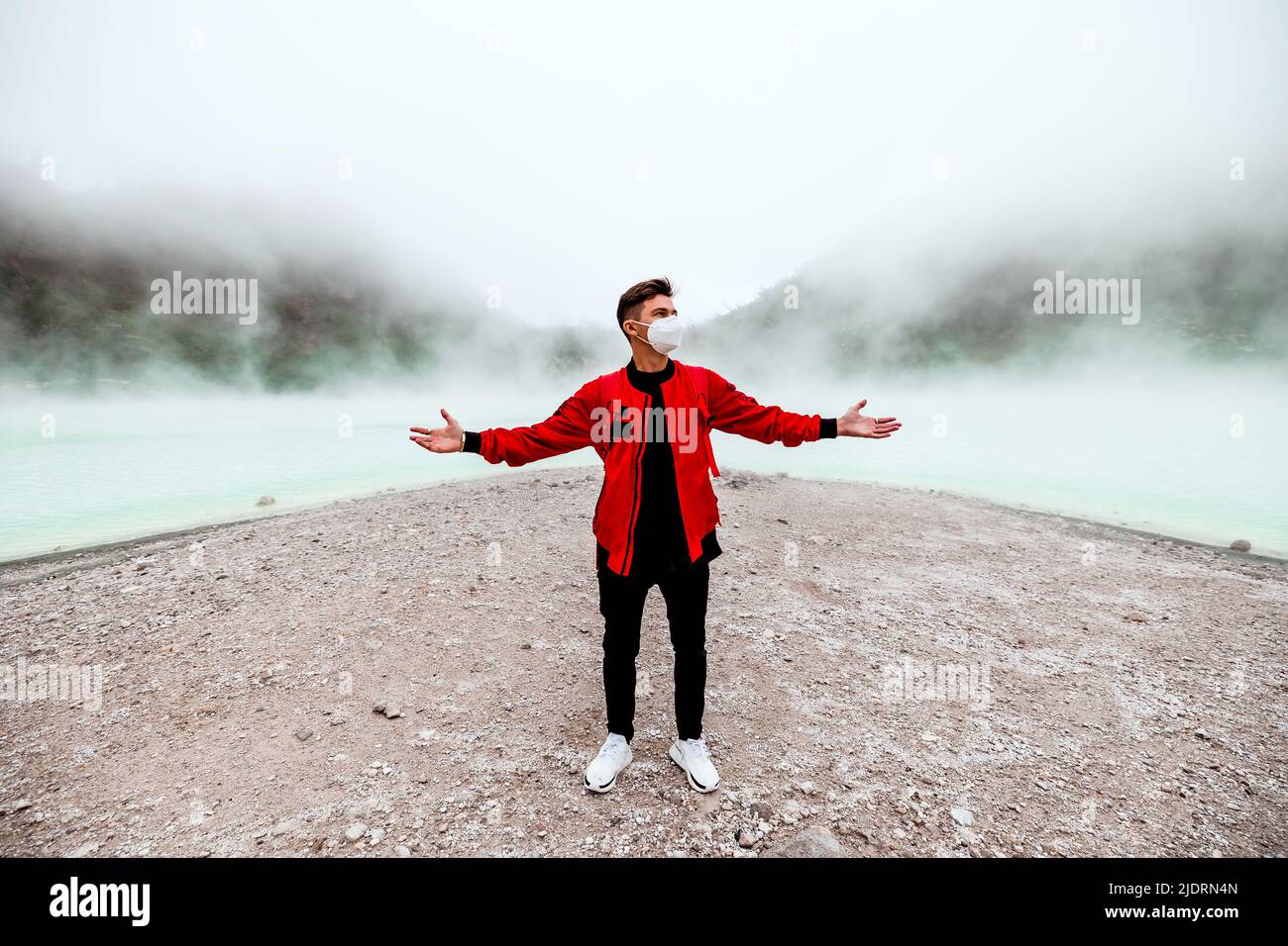 Giovane uomo in giacca bomber rossa in piedi al lago di kawah putih sulfer a Bandung Foto Stock