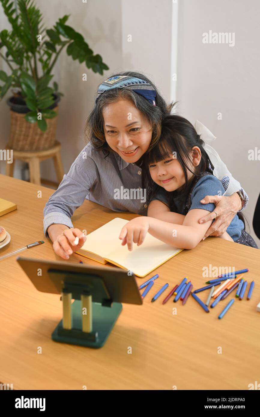 Nonna matura che aiuta il nipote piccolo che fa i compiti in linea. Concetto multi generazionale, familiare e d'amore Foto Stock