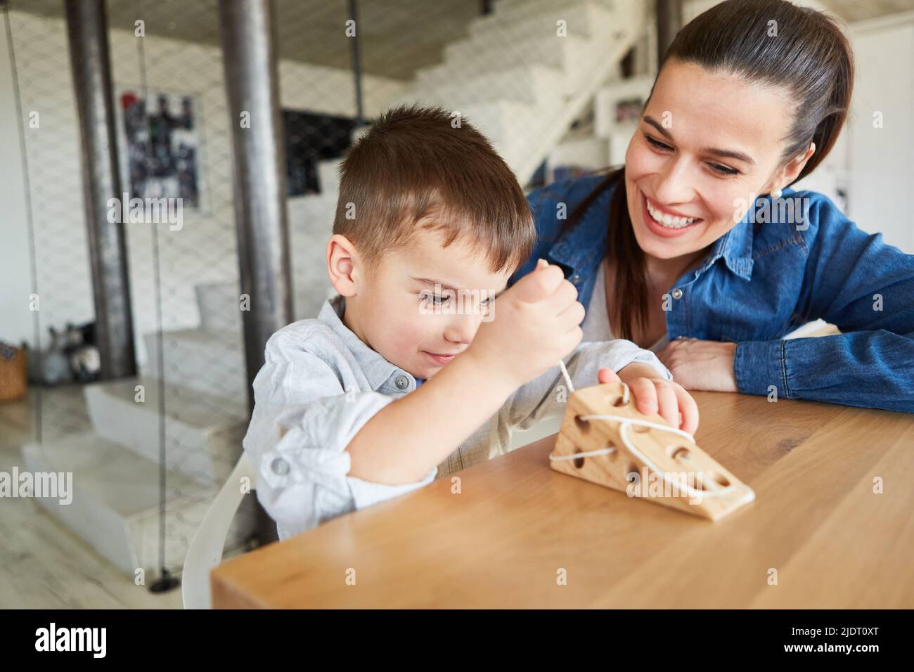 La madre guarda suo figlio infilando una corda su un giocattolo di legno Foto Stock