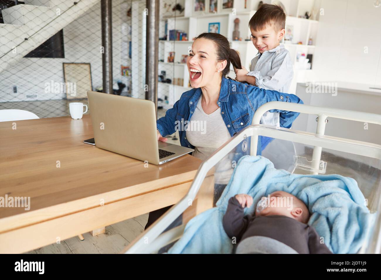 La madre del PC portatile dell'ufficio domestico è distratta dal bambino e disturbata durante una videoconferenza Foto Stock