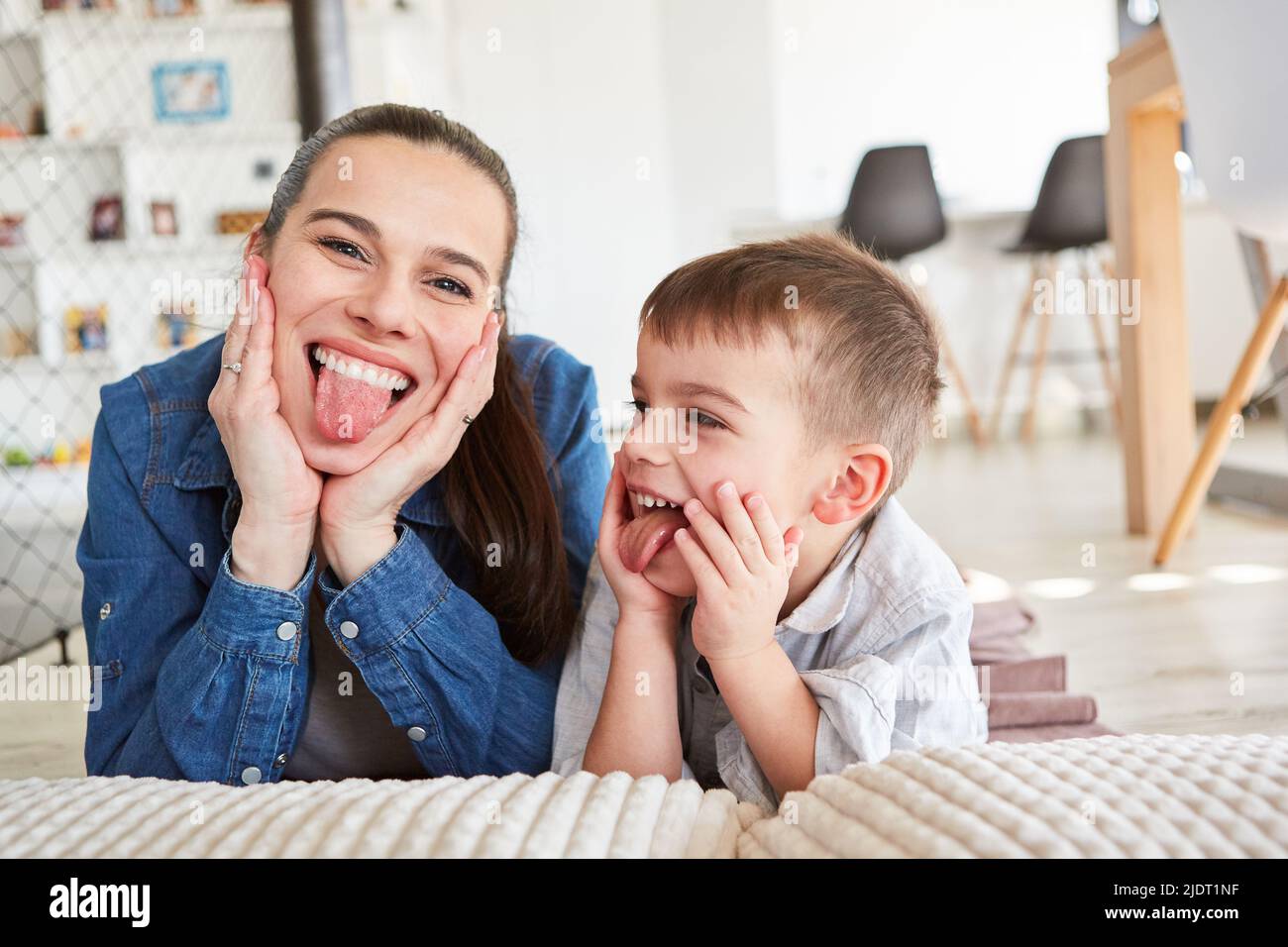 Madre e figlio che si trovano fianco a fianco e che attaccano le loro lingue a casa nel soggiorno Foto Stock