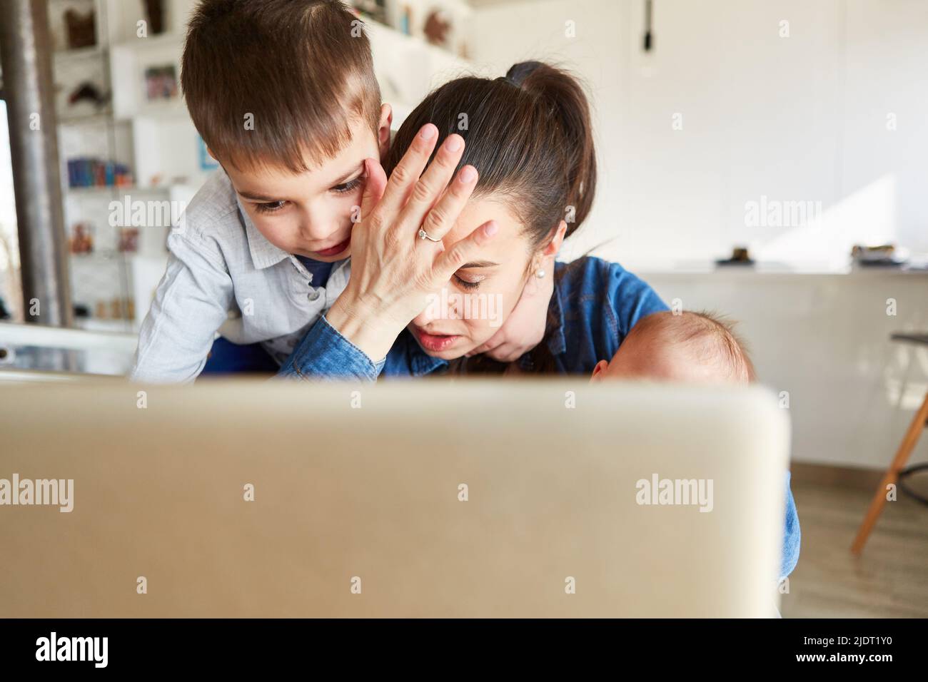 Madre single con burnout siede al computer in ufficio con il suo bambino e bambino Foto Stock