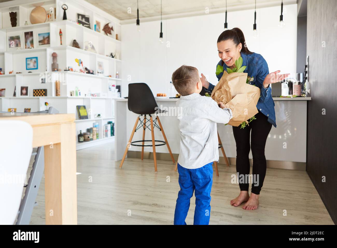 Il bambino sorprende la madre con un bouquet di fiori per un compleanno o la festa della mamma a casa Foto Stock