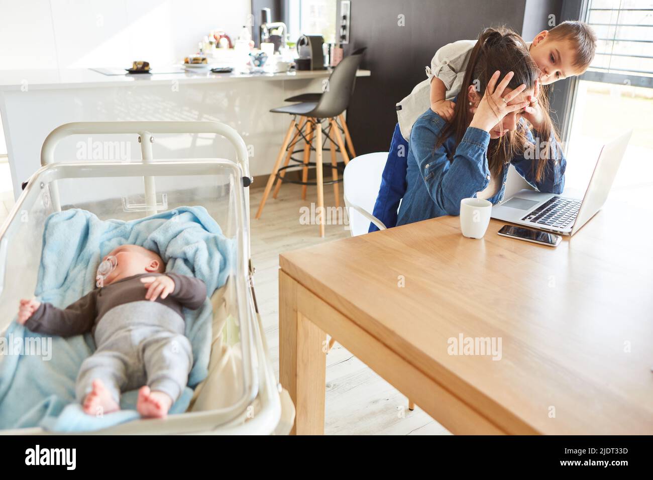 Madre sola con burnout in ufficio con bambino e bambino di fronte al computer portatile Foto Stock