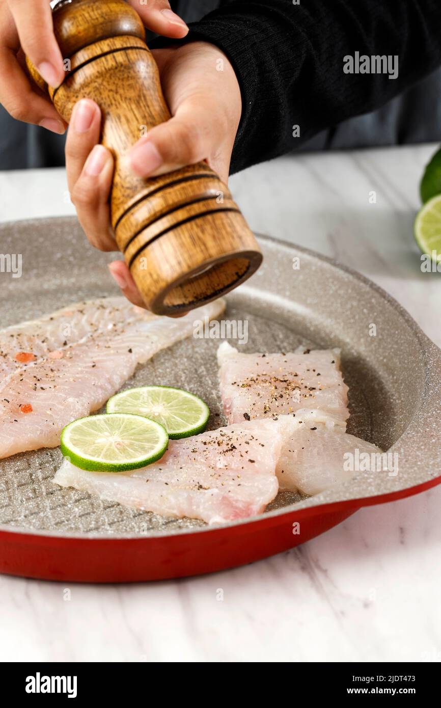 Donna Pepe macinazione a mano su Fish Filet su una padella utilizzando legno Pepe Mill, primo piano su Dori Filet Foto Stock