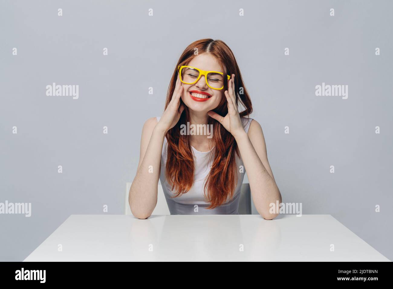 Ridendo Caucasian donna seduta al tavolo indossando occhiali giallo Foto Stock
