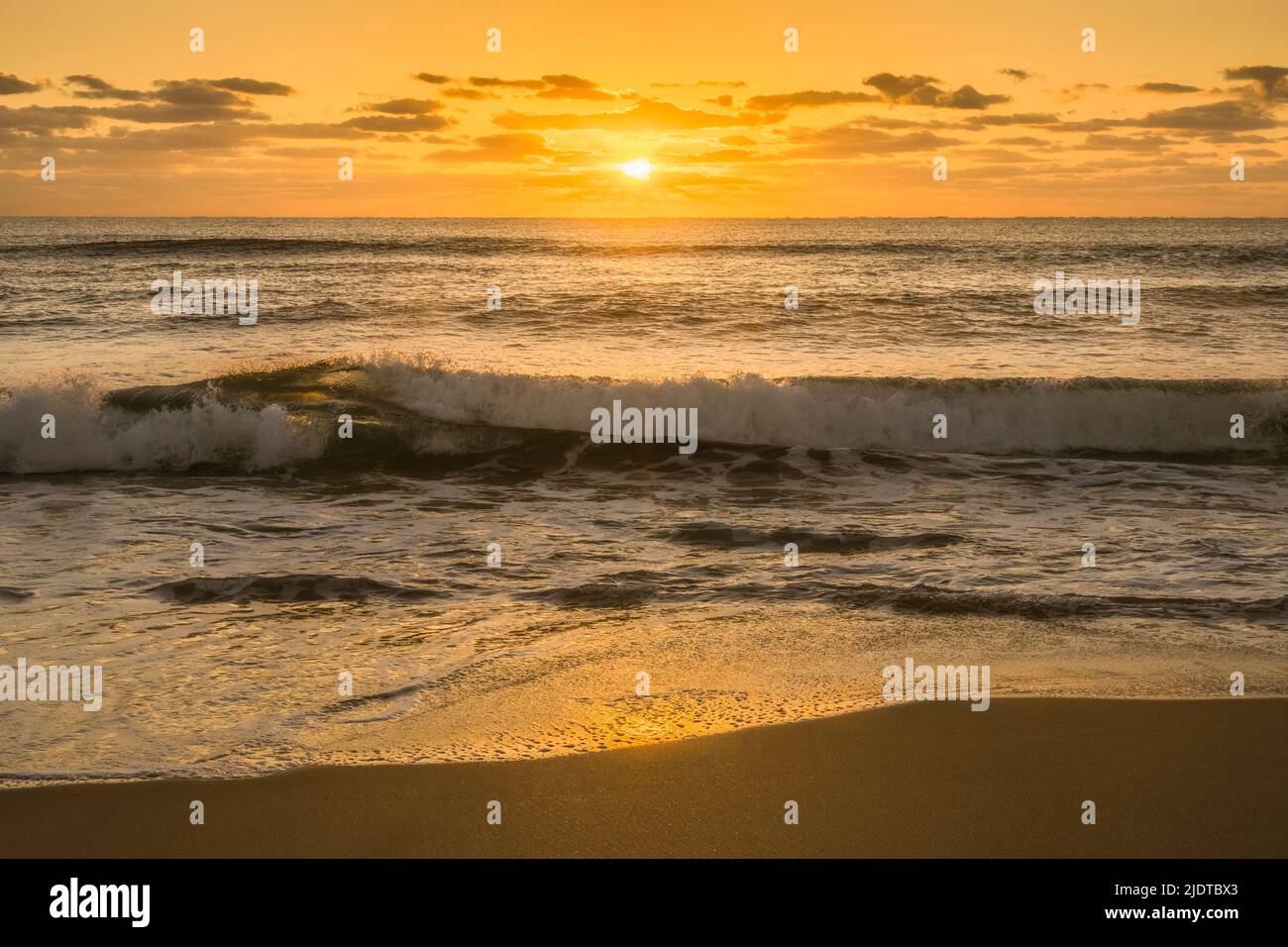 All'alba, la calma onda dell'oceano si infrange sulla spiaggia sabbiosa Foto Stock