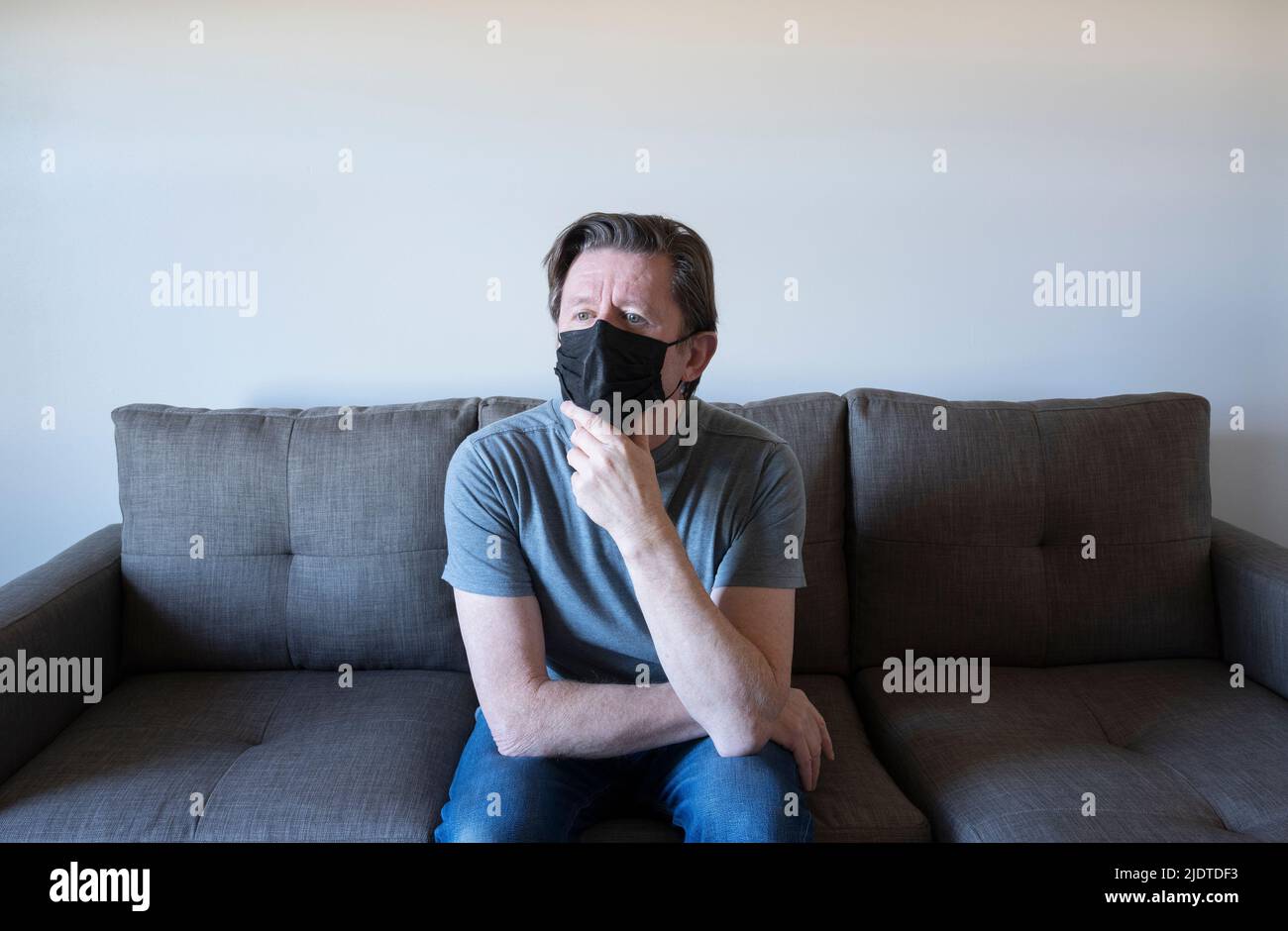 Uomo pensivo in maschera viso seduto sul divano Foto Stock