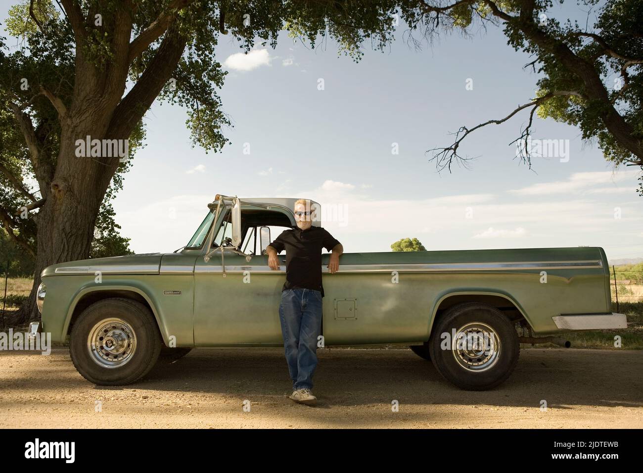 Uomo biondo (40-60 anni) con barba appoggiata su un pick up camion d'epoca parcheggiato in una zona rurale. Foto Stock