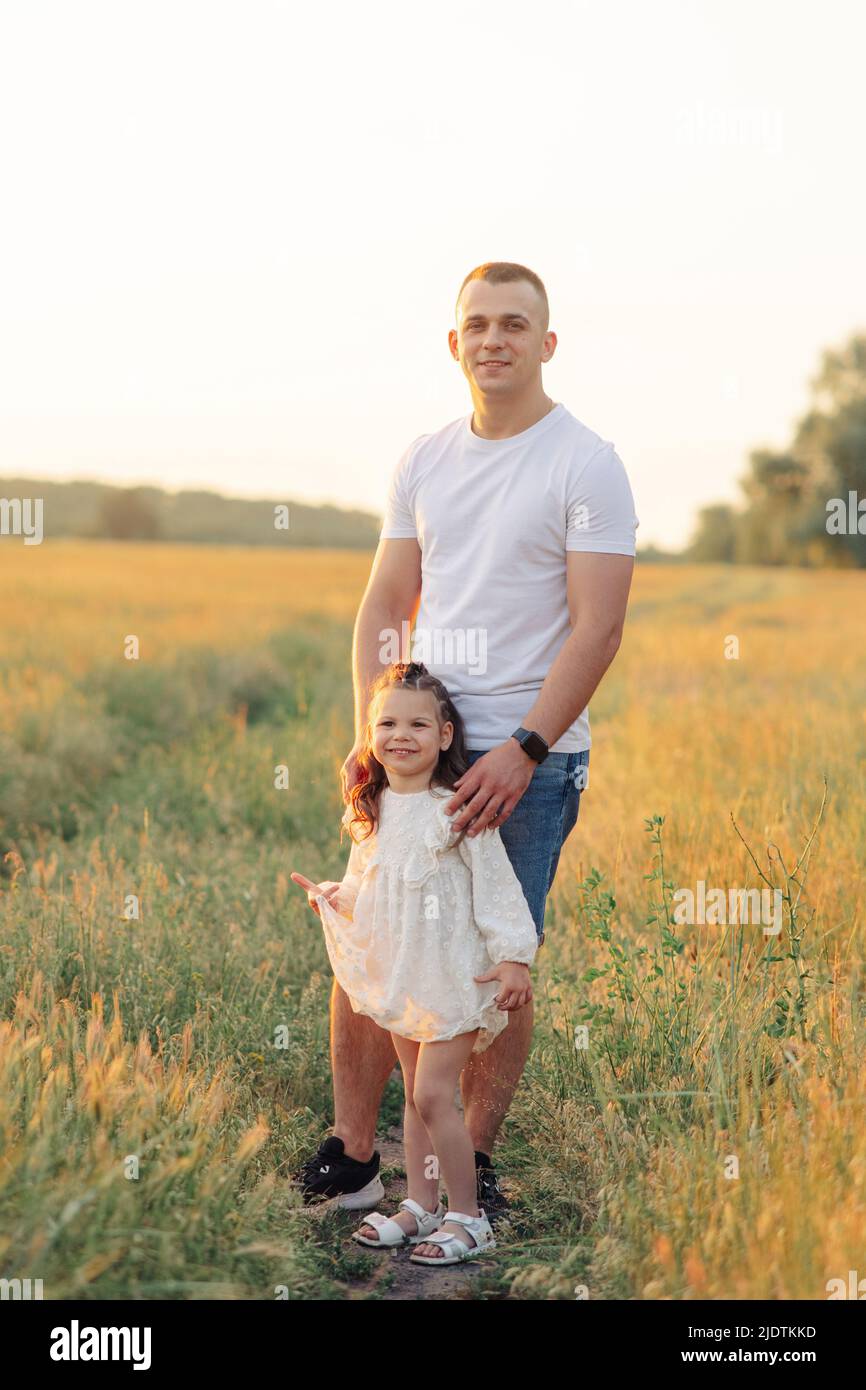 Felice padre cammina con la figlia tra prato al tramonto. Foto Stock