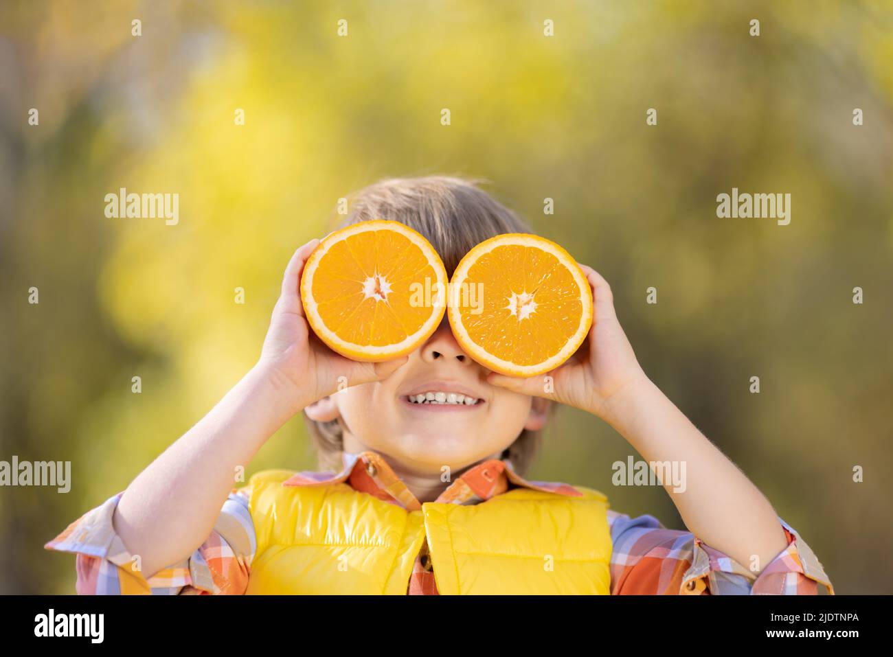 Sorprendo il bambino che tiene le fette di frutta arancione come gli occhiali da sole. Ragazzo divertente contro autunno sfocato sfondo. Felice ragazzo in autunno all'aperto. Eati sani Foto Stock