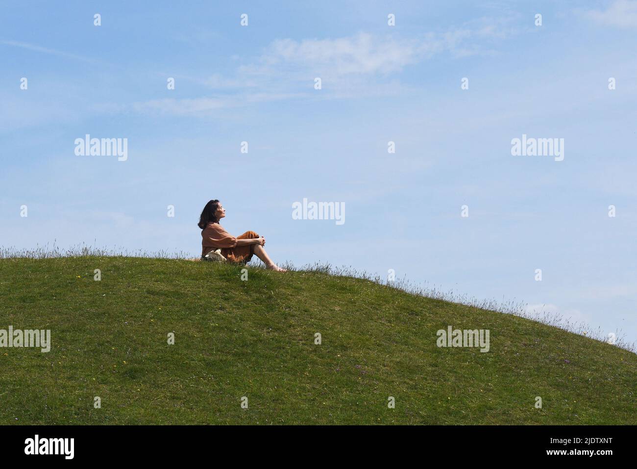 Una signora che si gode il sole di metà estate su una collina verde nel Wiltshire. Foto Stock