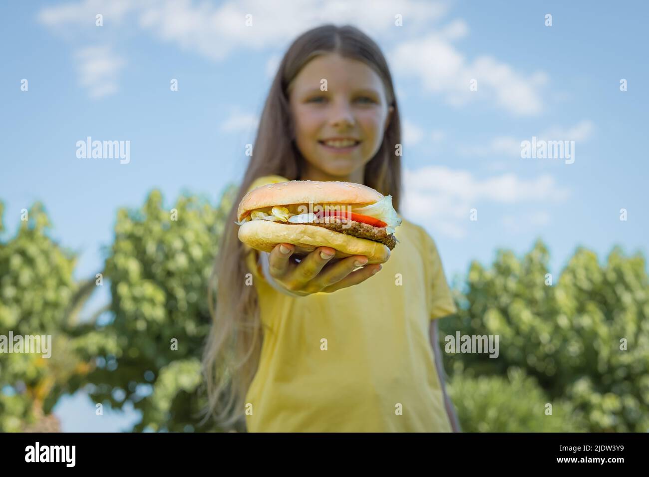 Una ragazza adolescente tiene fuori un hamburger con una cotoletta di manzo. Fuoco selettivo Foto Stock